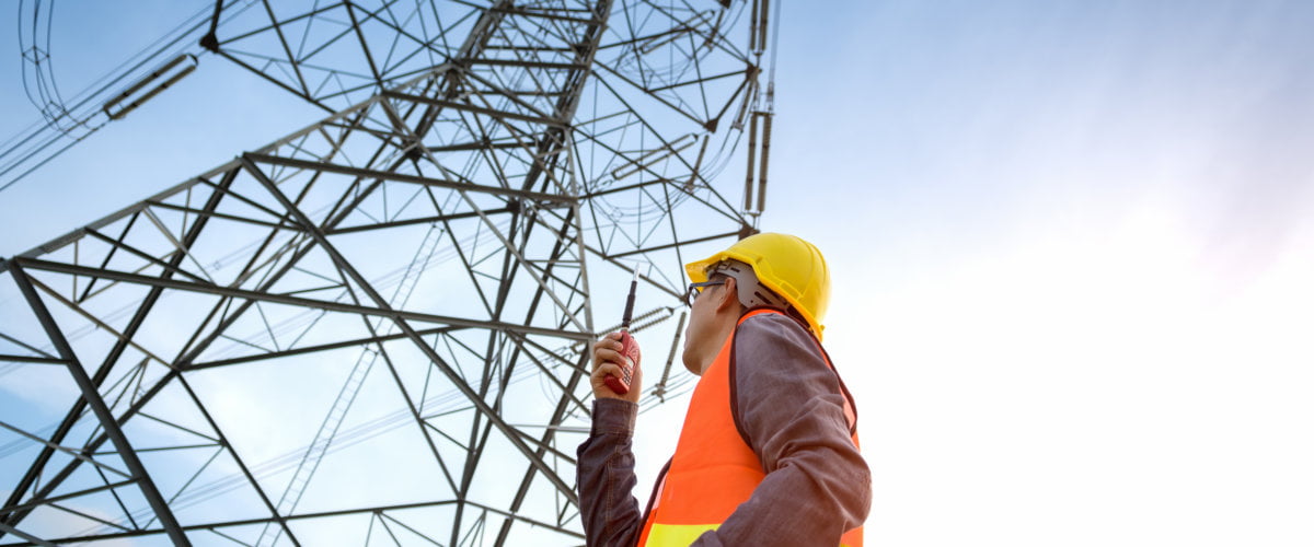 Photograph of lone working Utilities worker checking location site near to High voltage tower.