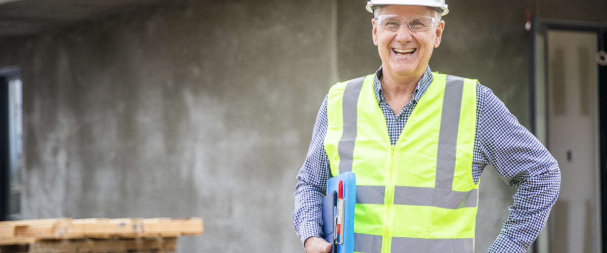 Photograph of a lone working senior construction site manager visually inspecting a building project.