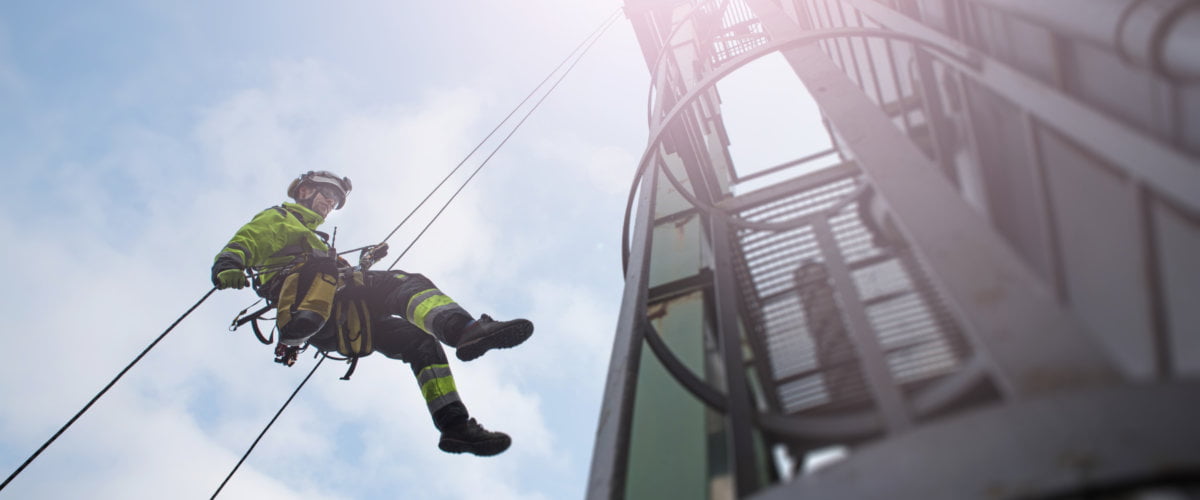 Photograph of lone worker using manual rope access to abseil from tower.