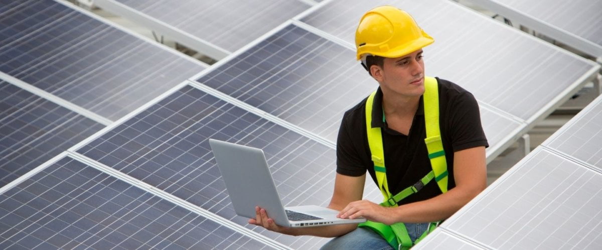 Photograph of lone working solar panel installer inspecting an array of panels