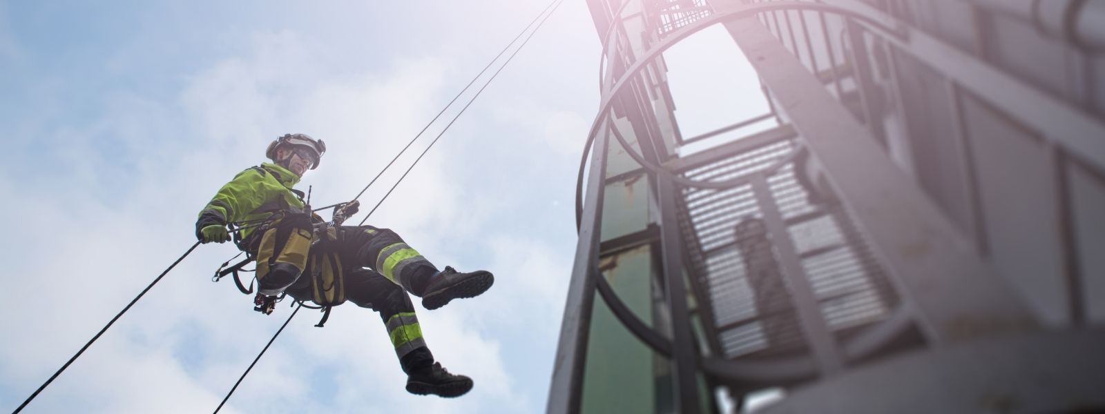 Photograph of lone worker using manual rope access to abseil from tower.