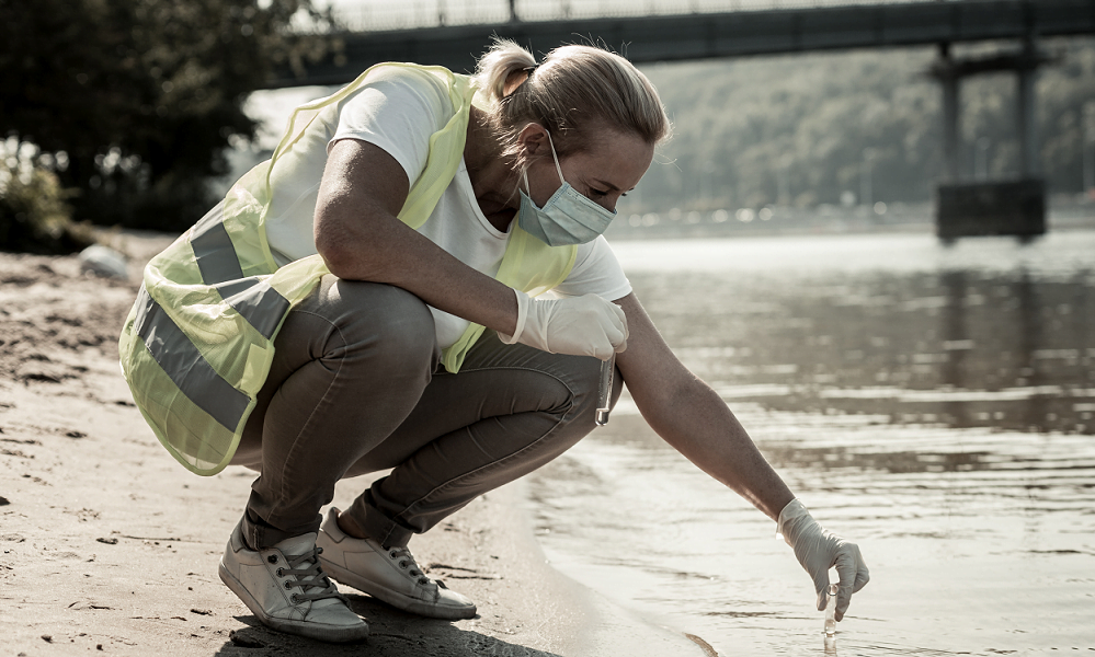 Image of a female lone worker undertaking a water inspection at a riverside.
