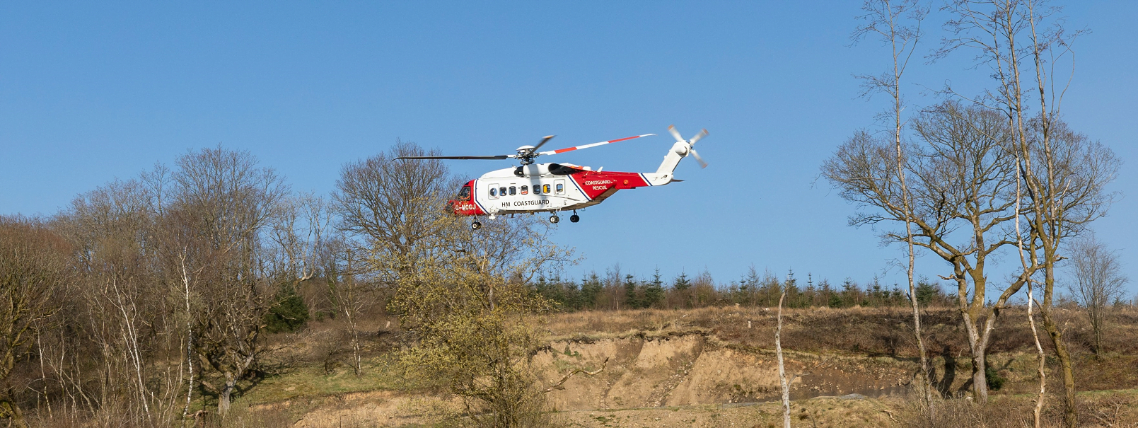 Photograph of HM Coastguard helicopter landing in remote area in UK. One of the Emergency Services which may be used in an emergency 999 situation. Image with thanks to Francois Olwage on unsplash.