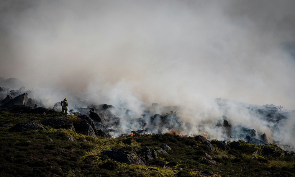 Photograph of a wildfire producing lots of smoke on Y Fron in Wales with a firefighter working to control the fire.