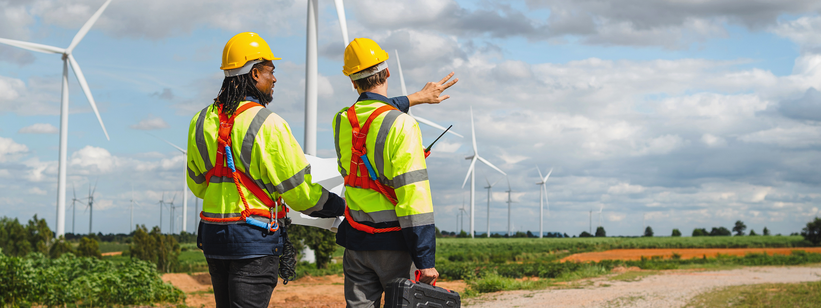 Photograph of two workers, wearing high visibility jackets and hard hats, operating a buddy system on an onshore windfarm site.